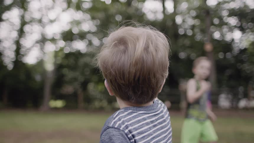 Toddler looks at a child swinging on a swing