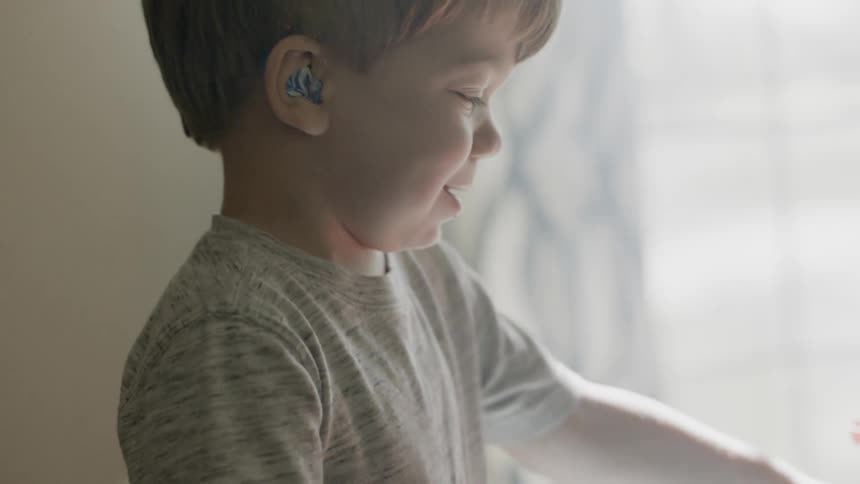 A boy wearing hearing aids is playing with toys inside in daylight