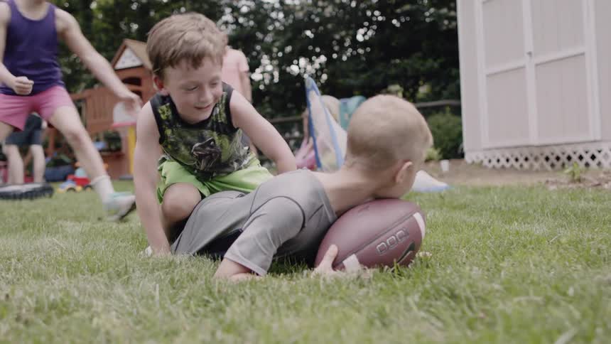 Children play with a football in a backyard