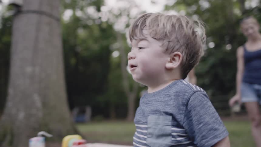 Woman talks to a toddler who takes off across a yard