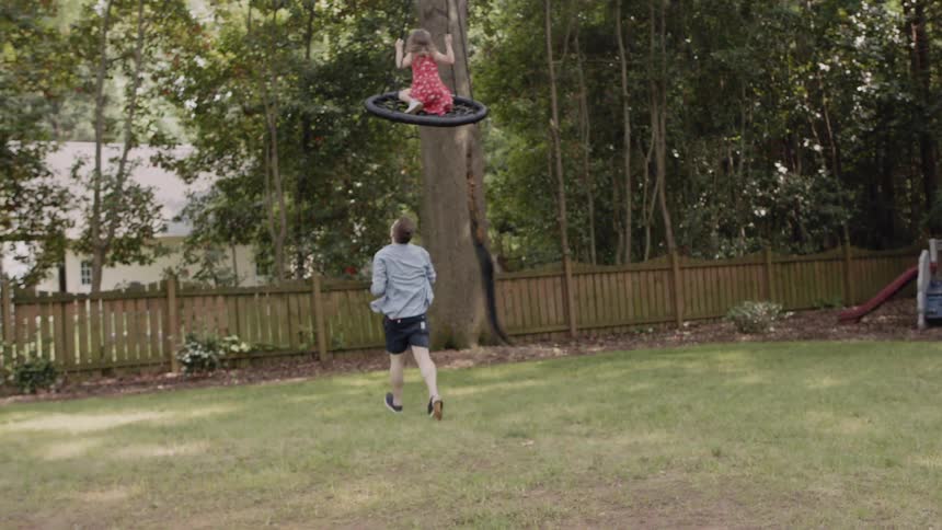 A father is pushing his daughter on a large swing