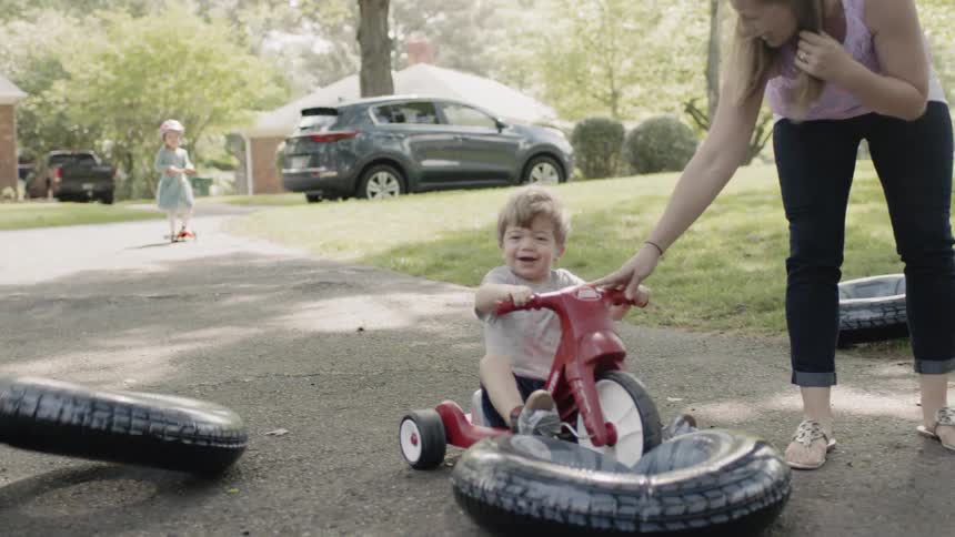 Toddler riding a tricycle knocks over a stack of inflatable rings