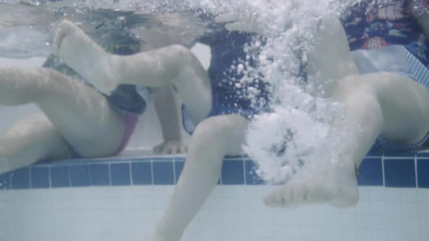 Three kids kicking their legs under water