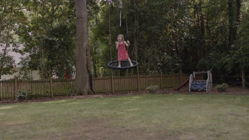 A little girl is riding on a swing in a backyard during the day