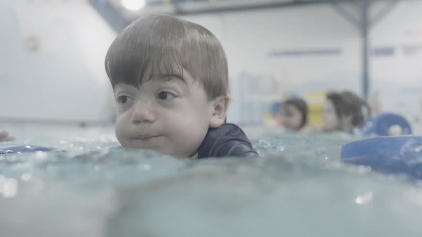 Child floats in a pool being held up by an adult