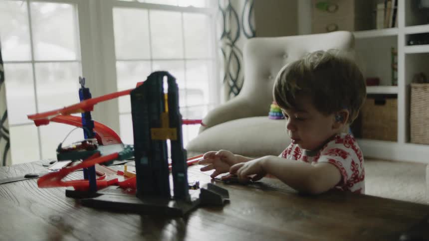 A boy is playing with toy cars and a race set on a table inside in daylight