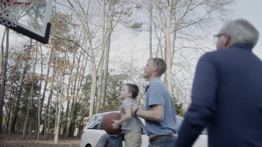 Men and children play basketball in a driveway