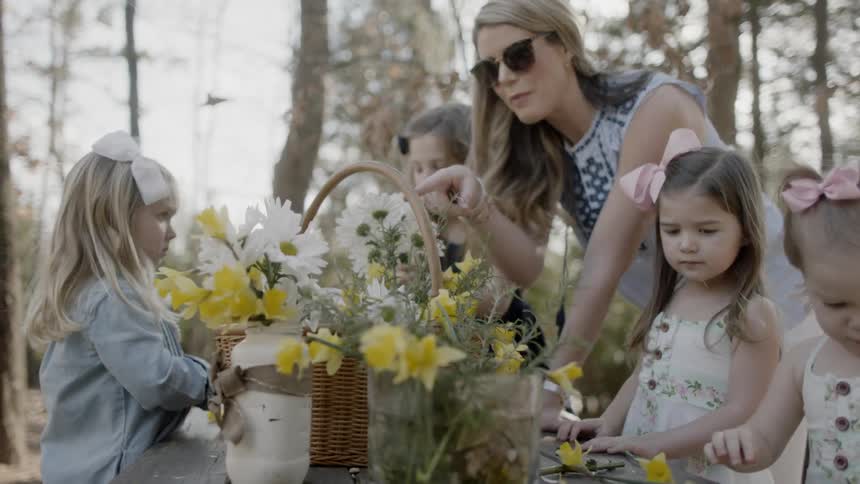 A woman helps girls arrange bouquets from a basket of cut flowers