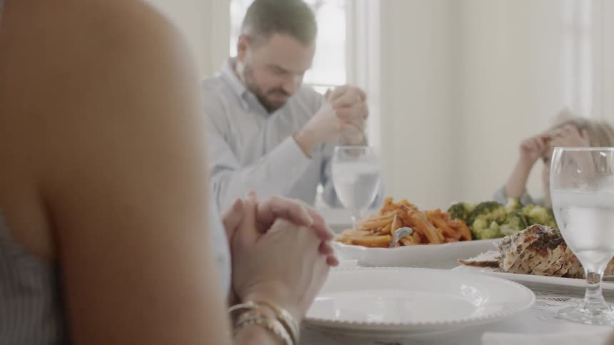A man is saying a prayer at a family dinner inside during the day