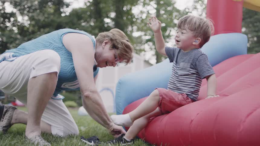 Toddler sits as a woman puts shoes on his feet