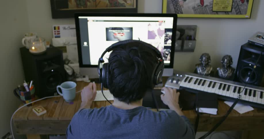 Man wearing headphones types on a keyboard looking at a monitor