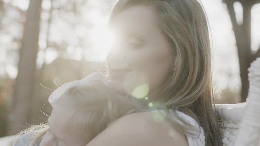 Woman and girl cuddle outside at sunset