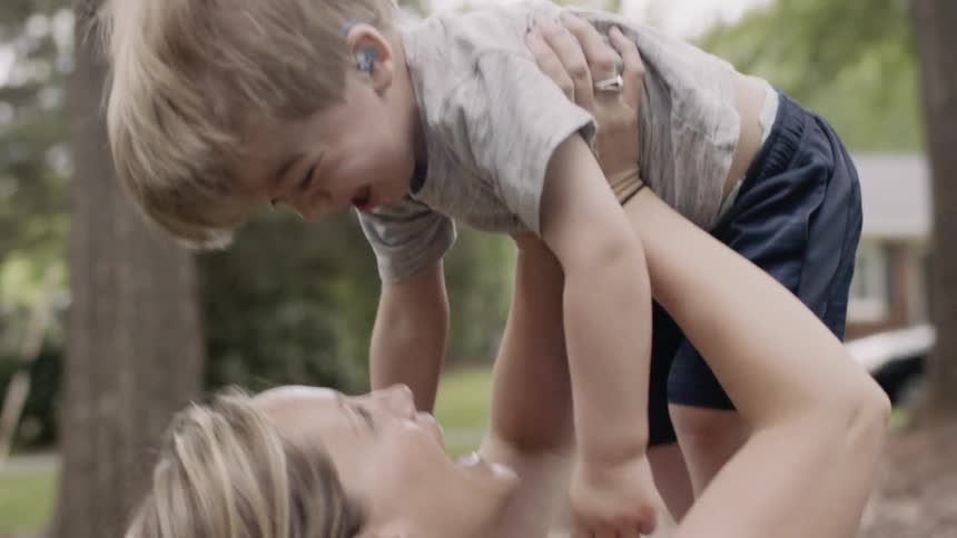 Woman holds a toddler up in the air outside in a yard