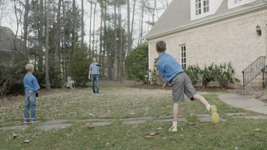 Man and two children throw a ball in a yard