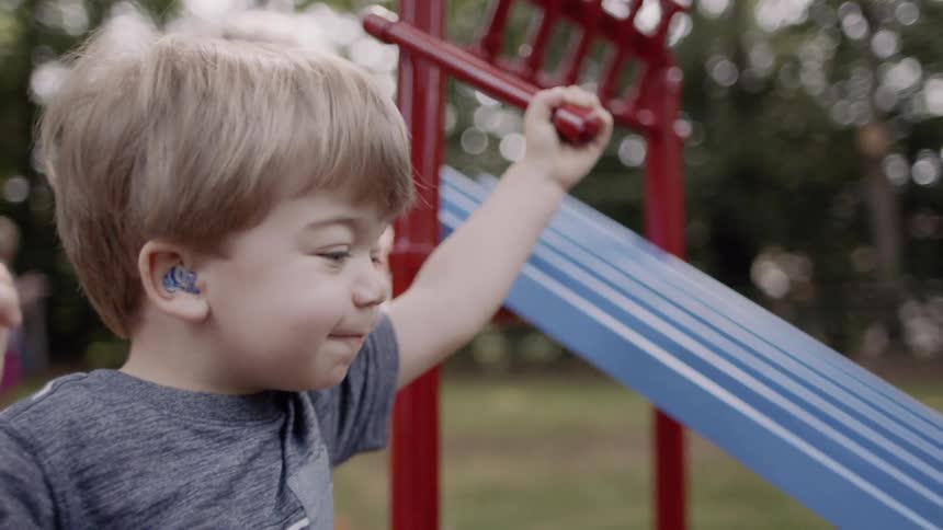 A boy is releasing toy cars down a slide outside in a backyard in daylight