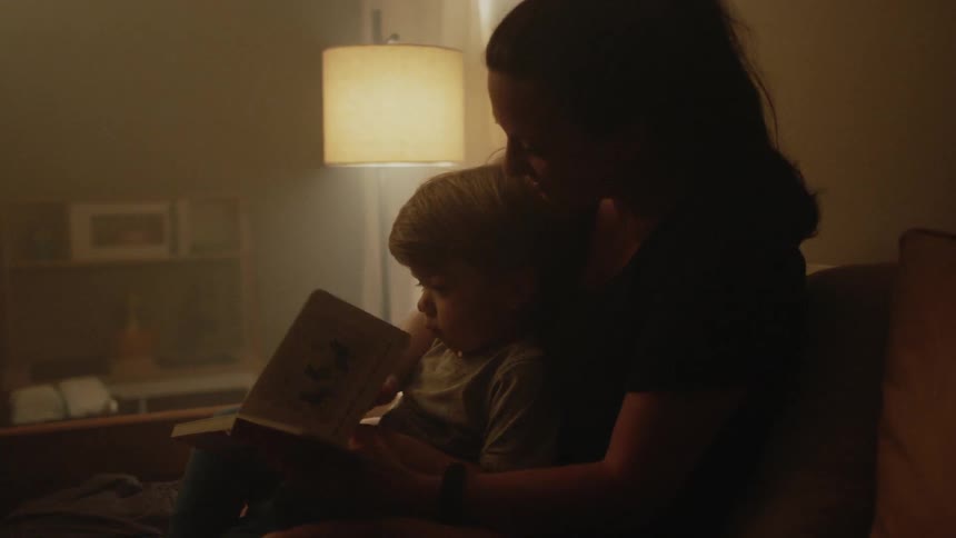 Person reads to a toddler in a dimly lit room