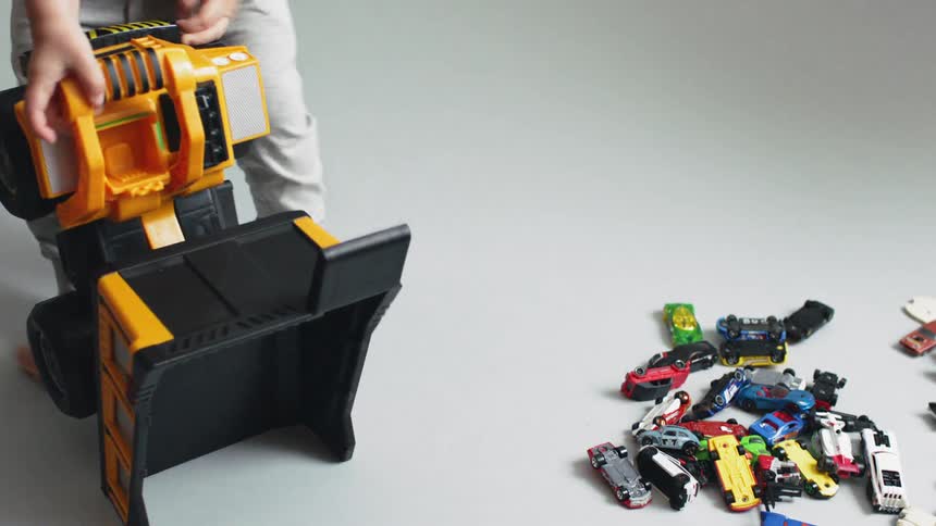 A boy is dumping a load of toy cars from a toy dump truck
