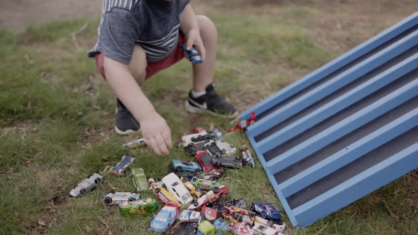 Child plays with toy cars outside in a yard