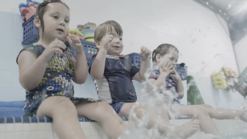 Children sitting on the edge of a pool kick their feet and splash