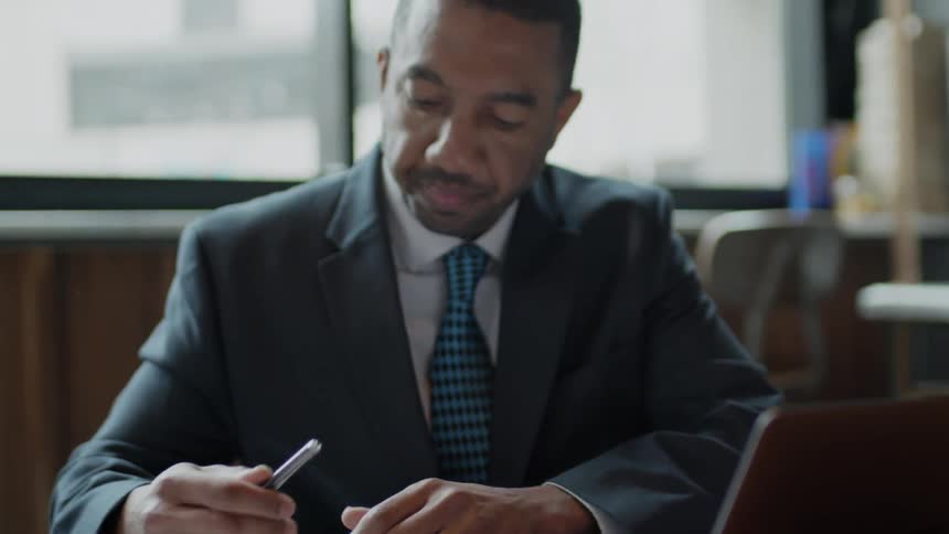 Businessman types on a laptop and takes notes