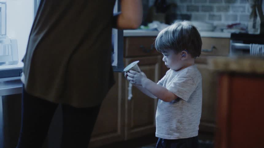 Woman hands a young boy a cup as they stand in the kitchen
