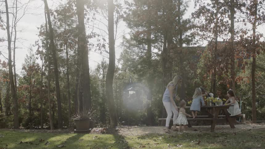 The children and woman jump on the table with flowers in the yard