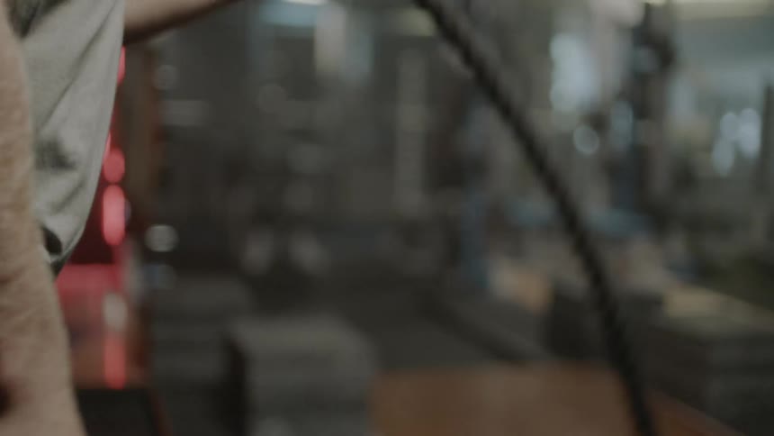 A man is exercising in a gym pulling ropes