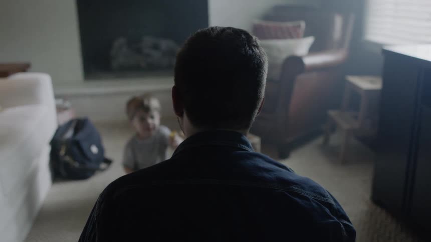 A man is sitting on the floor of his living room playing with his son