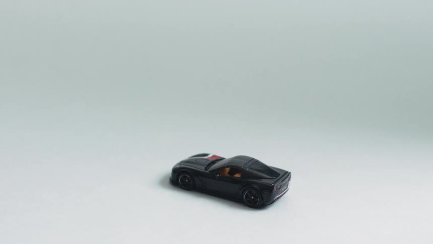 A black hot wheels car sits on a white surface