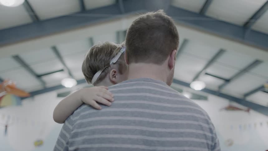 A boy pushes his swim goggles up on his head while his dad holds him