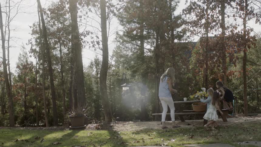Three young girls gather at a picnic table as a woman approaches