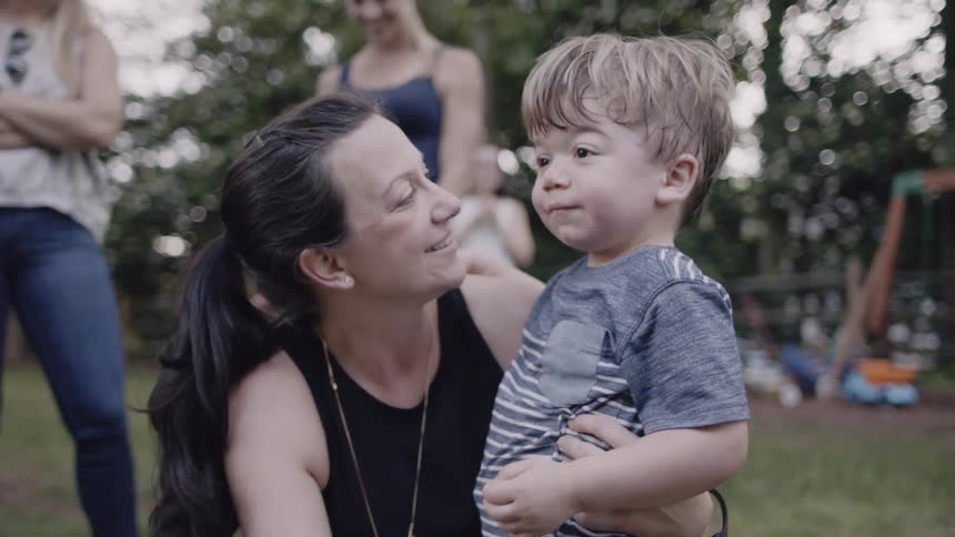 Toddler runs into a woman's arms who smiles and talks to him