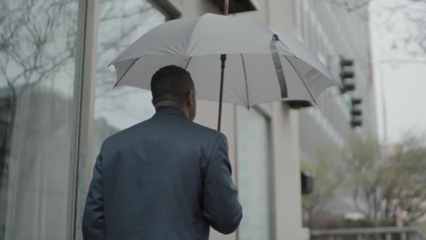 Man walks down the sidewalk as he holds an umbrella