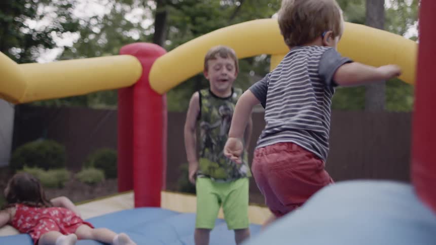 Children are playing on a bouncy castle in a backyard in daylight