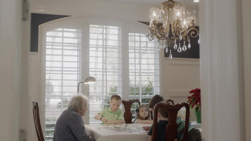 An elderly woman and young boys do a puzzle at a dining table