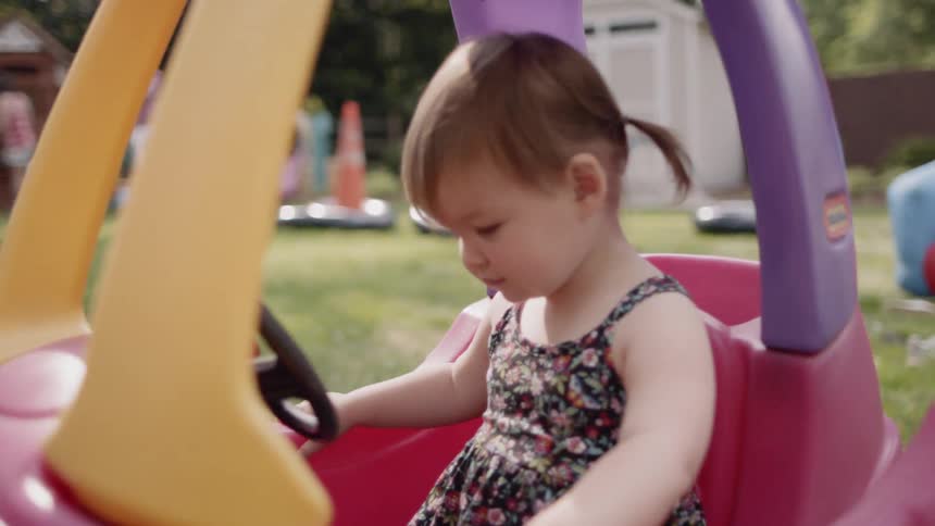 Children play in the backyard and one sits in a toy car