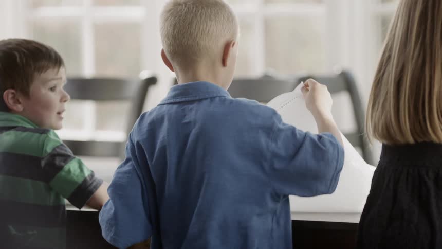 Young children fold napkins at a dining table