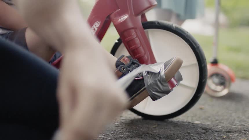 Adult tapes a child's shoe to a bike pedal