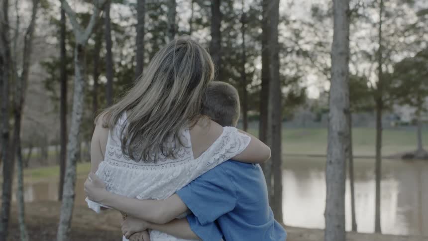 Woman hugs two boys next to a lake