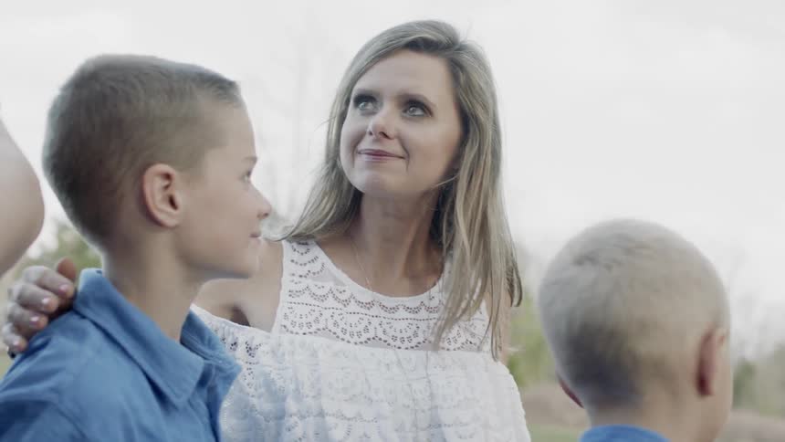 Mother smiles and hugs her two sons while outside