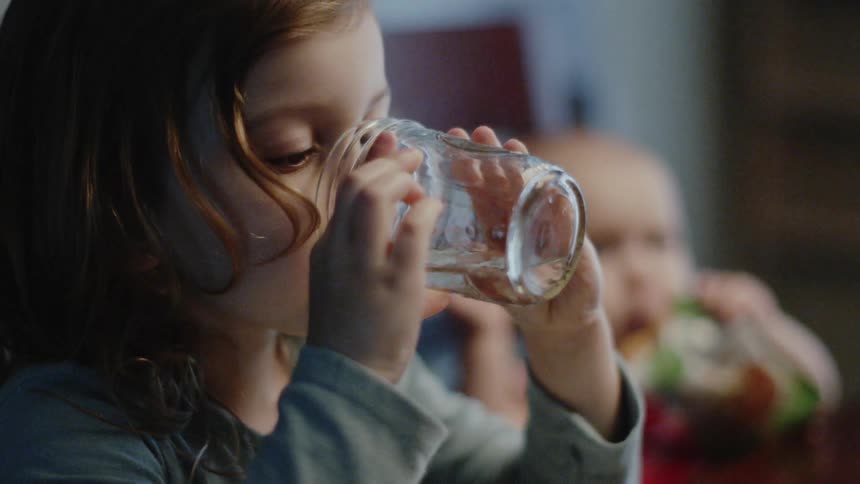 Young girl drinks water from a clear glass
