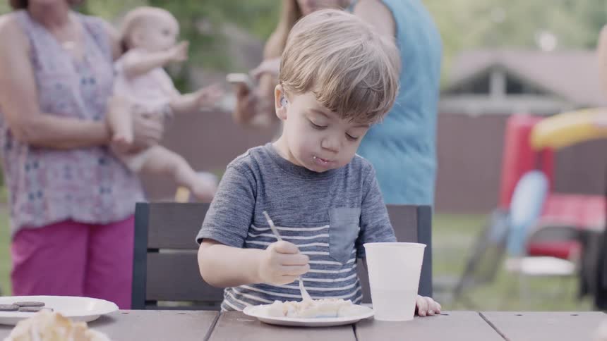 Toddler eating at a picnic table outside near adults