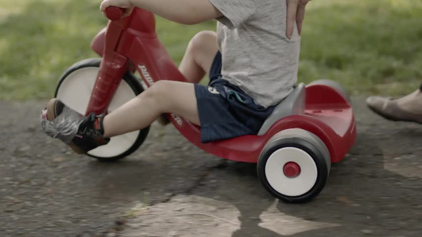 A boy is learning to ride a tricycle outside in daylight