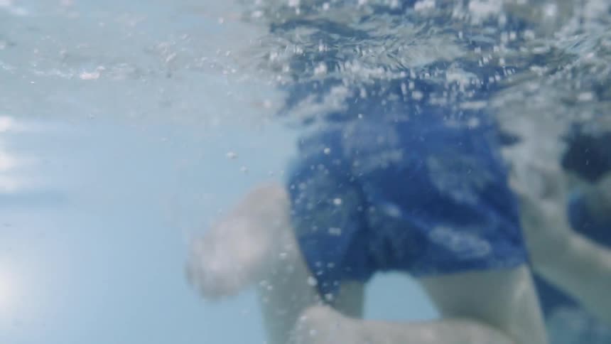 Little boy is kicking his legs underwater and learning to swim