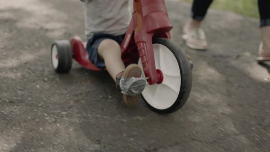 Toddler rides a trike as a woman walks next to him
