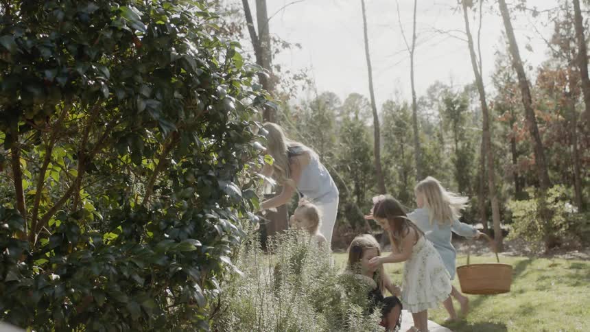 Woman and several children outside near bushes