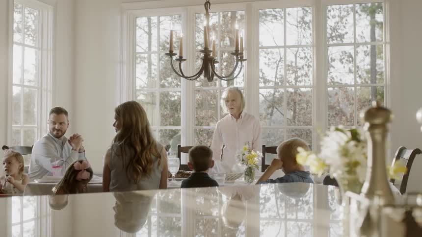 A family is gathered around a dinner table waiting for a meal during the day