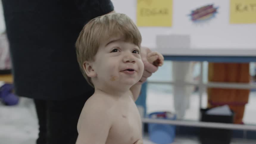 Young toddler turns around and smiles as he holds an adult's hand