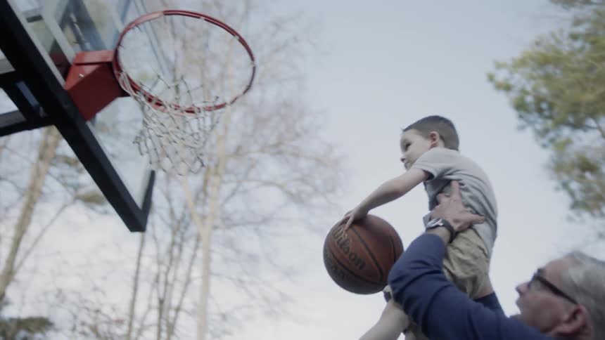 Man lifts a young boy up to a basketball hoop