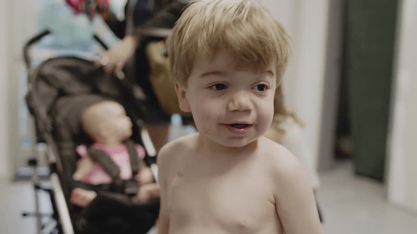 A dad helps his son take off his shirt then walks into the next room with him